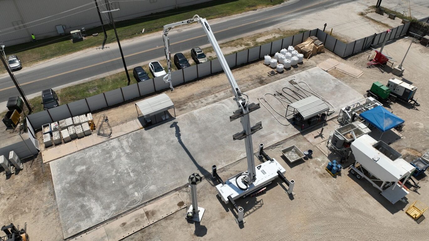 Overhead view of an ICON Titan printing system set up on a concrete slab beside hoppers, material bags and support equipment.