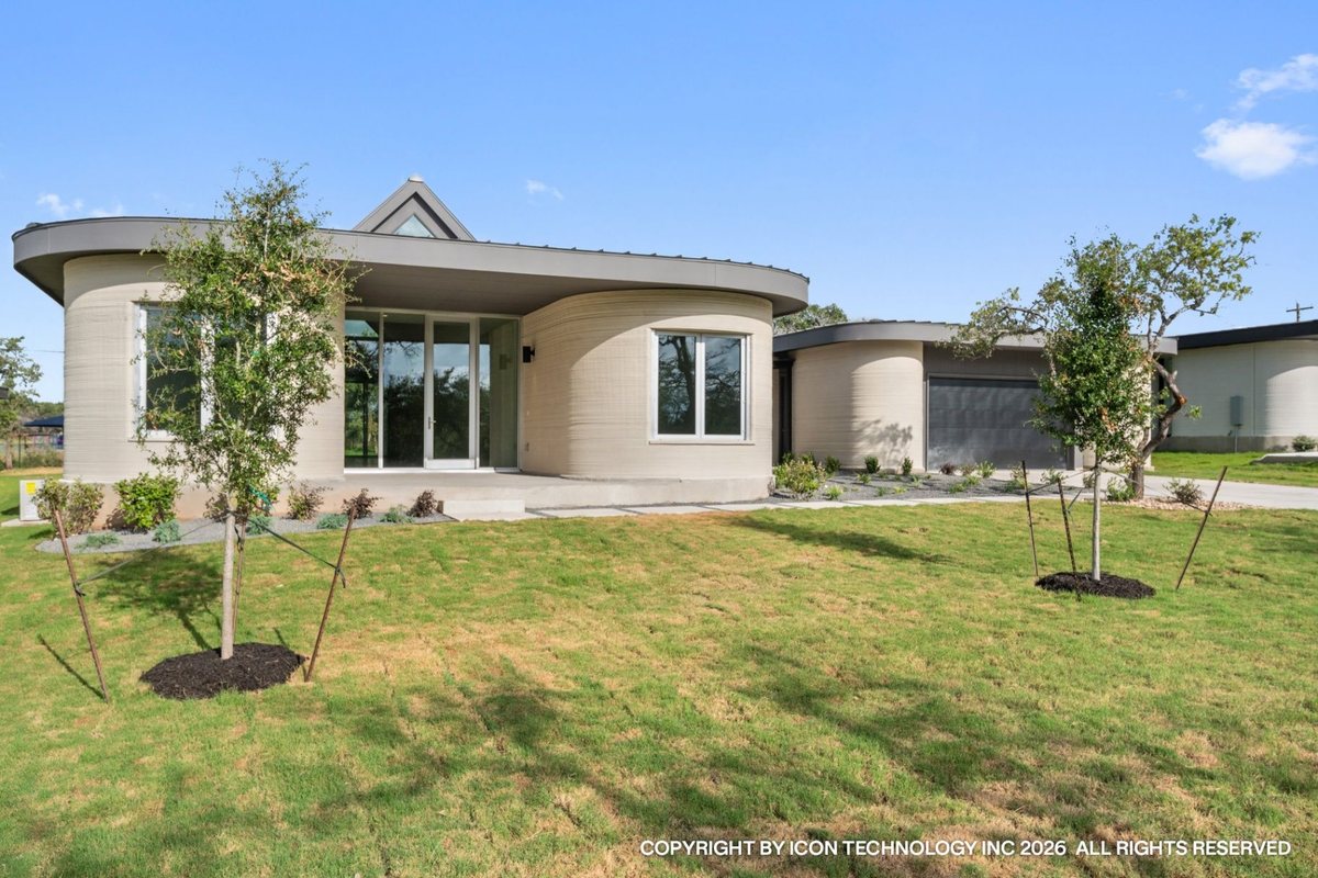 A single-story ICON-printed concrete home with curved printed walls, large glazing and a landscaped front lawn.